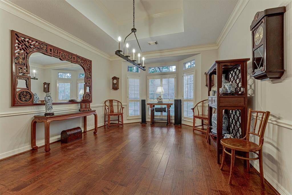 This elegant over-sized dining room features rich hardwood flooring, and a recessed ceiling and stylish light fixture.  The space is well-lit with natural light from the bay windows with plantation shutters, creating a warm and inviting atmosphere.