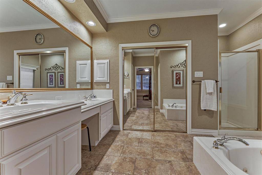 This spacious primary bathroom features dual sinks with ample counter space, a large mirror, a glass-enclosed shower, and a separate bathtub. The neutral tones and tile flooring add a touch of elegance, while the mirrored closet doors enhance the room's brightness.