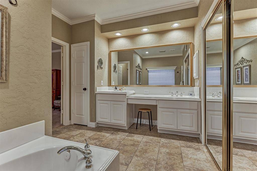 This spacious bathroom features a large vanity with dual sinks, and ample counter space, complemented by elegant lighting and a wide mirror. The neutral tones and tiled flooring create a warm, inviting atmosphere. A luxurious bathtub adds a touch of relaxation, while the mirrored closet doors enhance the sense of space.