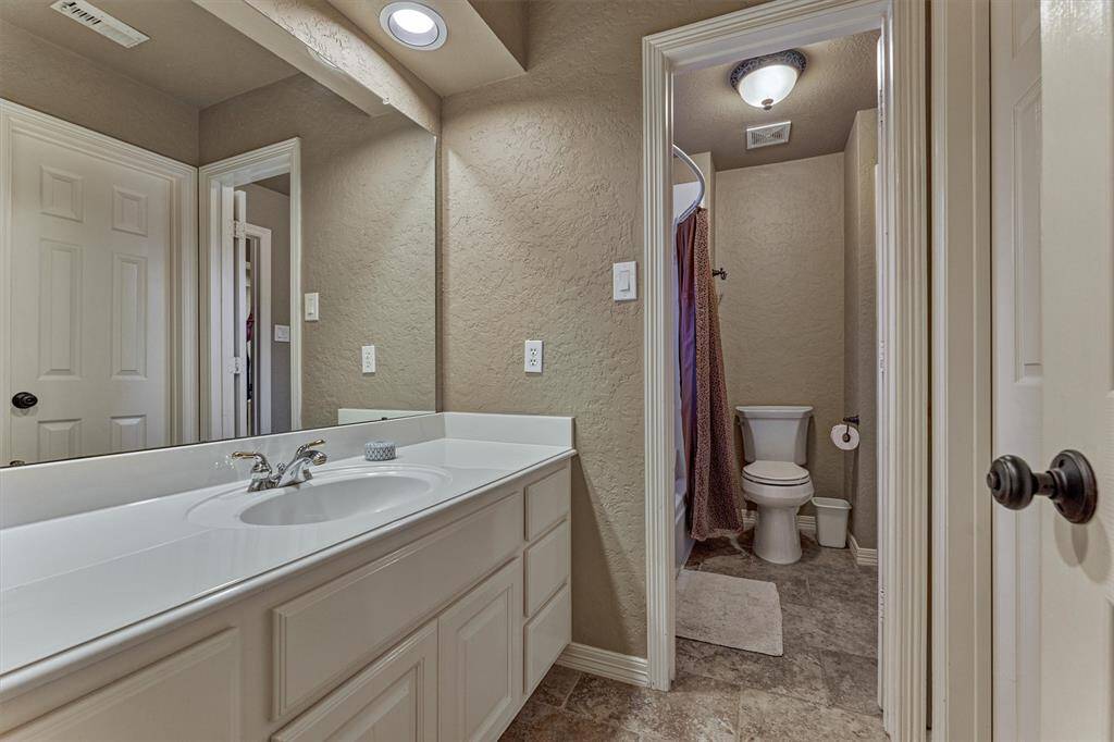 This photo showcases a secondary bathroom with a single-sink vanity, ample counter space, and a mirror. The room features a separate area for the toilet and shower, with neutral-toned walls and flooring, creating a clean and functional space.