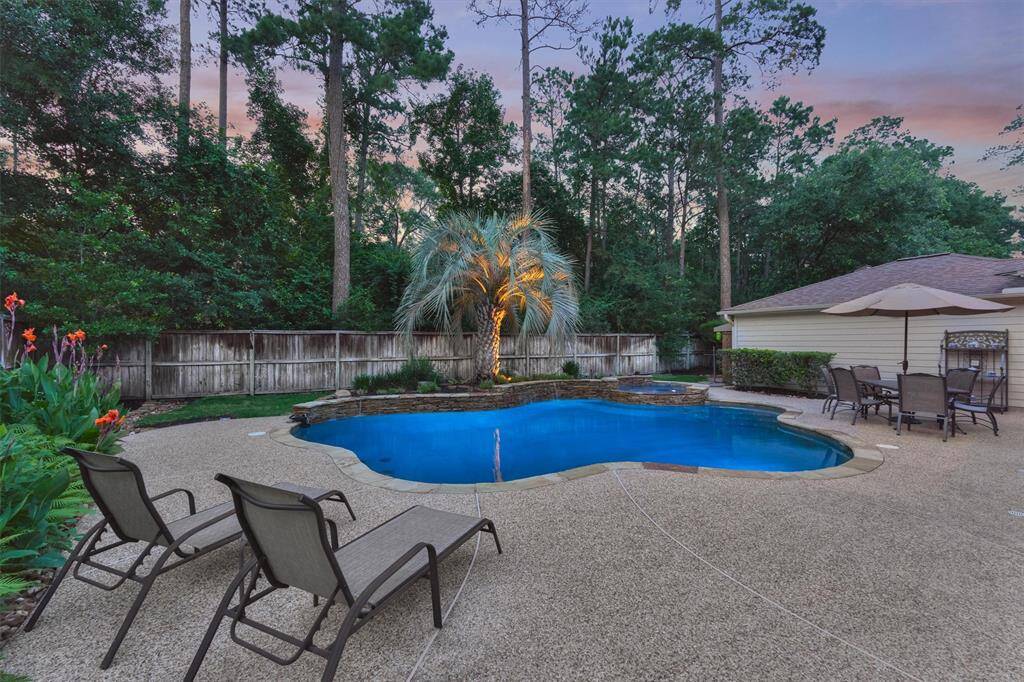 This photo showcases a serene backyard with a beautifully landscaped pool area, surrounded by lush greenery and tall trees for privacy. The pool is complemented by a spacious patio perfect for relaxation and entertaining.