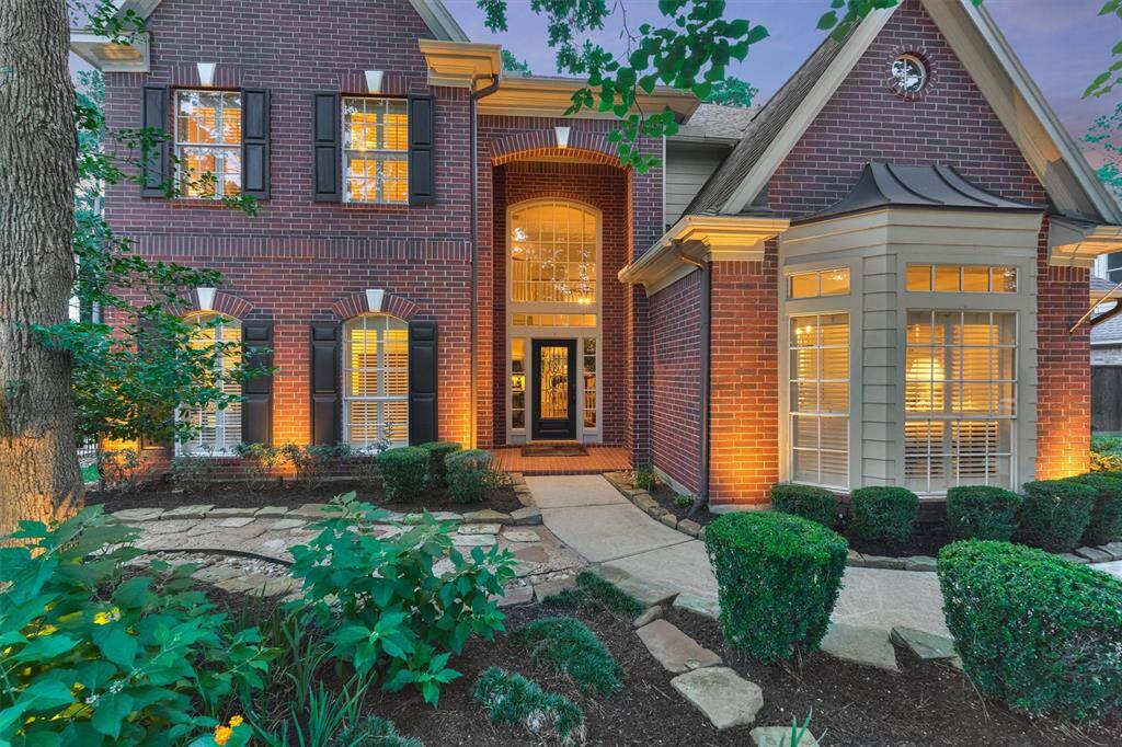 This beautiful brick home features elegant architectural details with a welcoming entryway, large windows with shutters, and well-maintained landscaping. The exterior lighting highlights the homes charm, creating a warm and inviting atmosphere.