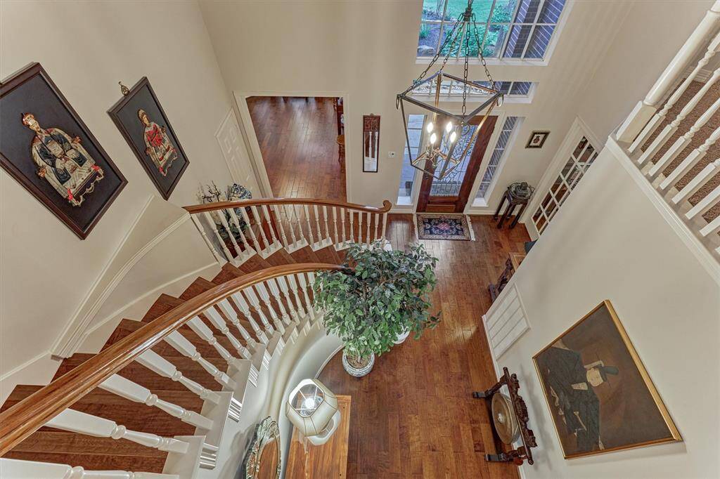 This photo showcases a grand foyer with a sweeping staircase featuring elegant wood and white railings. The space is adorned with a large chandelier and neutral paint pallet, creating an inviting and sophisticated atmosphere. Hardwood floors and large windows provide natural light, enhancing the welcoming entryway.