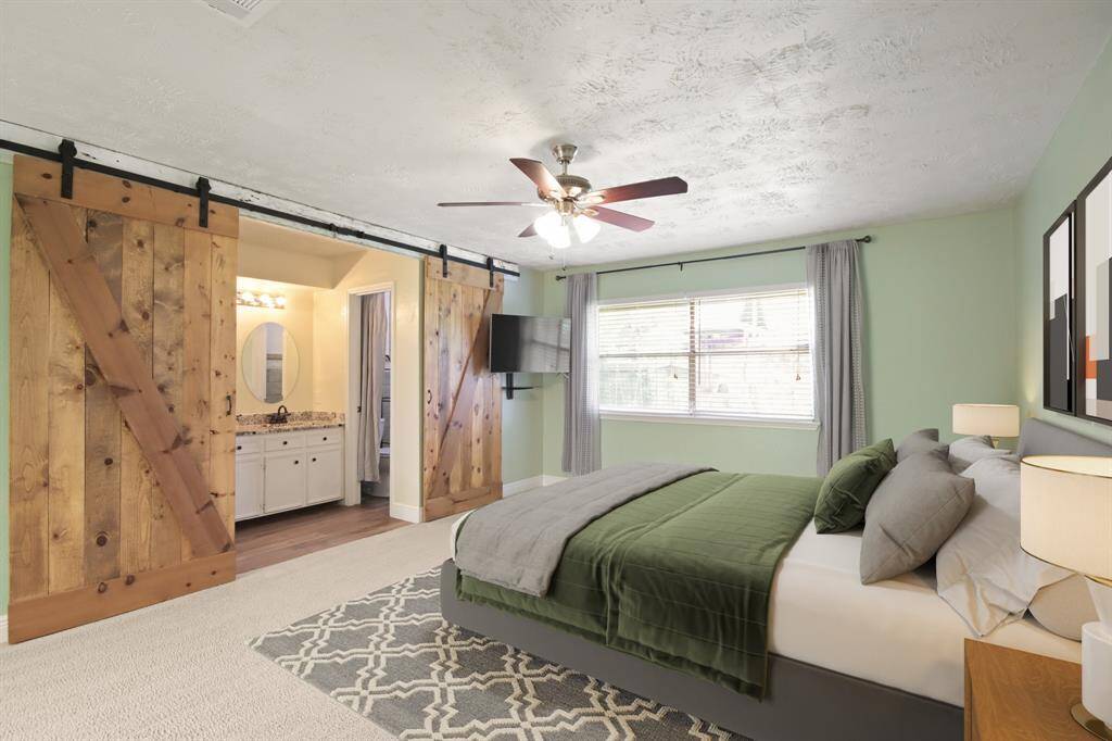 Virtually Staged: This magnificent primary suite features plush carpet, a ceiling fan, large windows with privacy blinds, and gorgeous barn doors.