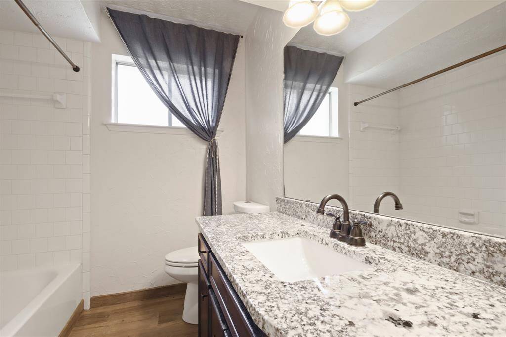 Secondary bathroom, featuring wood tile floors, a shower/tub combo, granite countertops, and a large mirror.