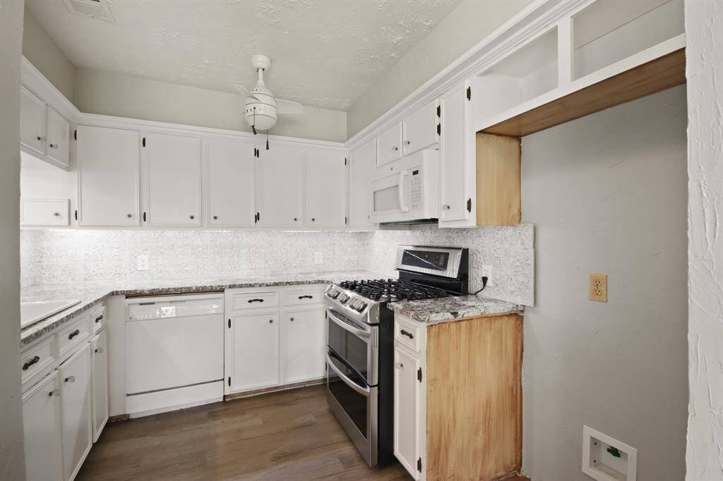 This beautiful kitchen features wood tile floors, white cabinetry, granite countertops, and tile backsplash.