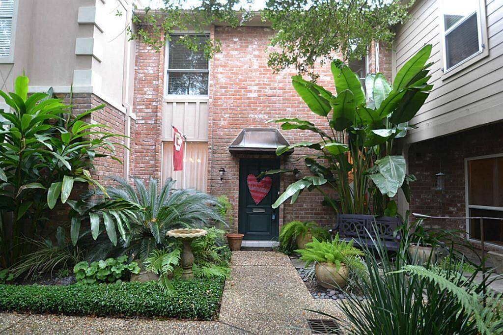 Charming courtyard entrance with lush greenery, brick exterior, and a cozy atmosphere. Features a quaint pathway, potted plants, and a decorative bench, offering a serene, welcoming vibe.