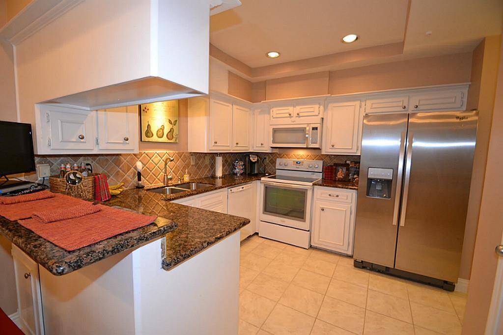 This kitchen features modern appliances, white cabinetry, granite countertops, and a tiled backsplash. It includes a large stainless steel refrigerator and ample lighting, creating a bright and functional space.