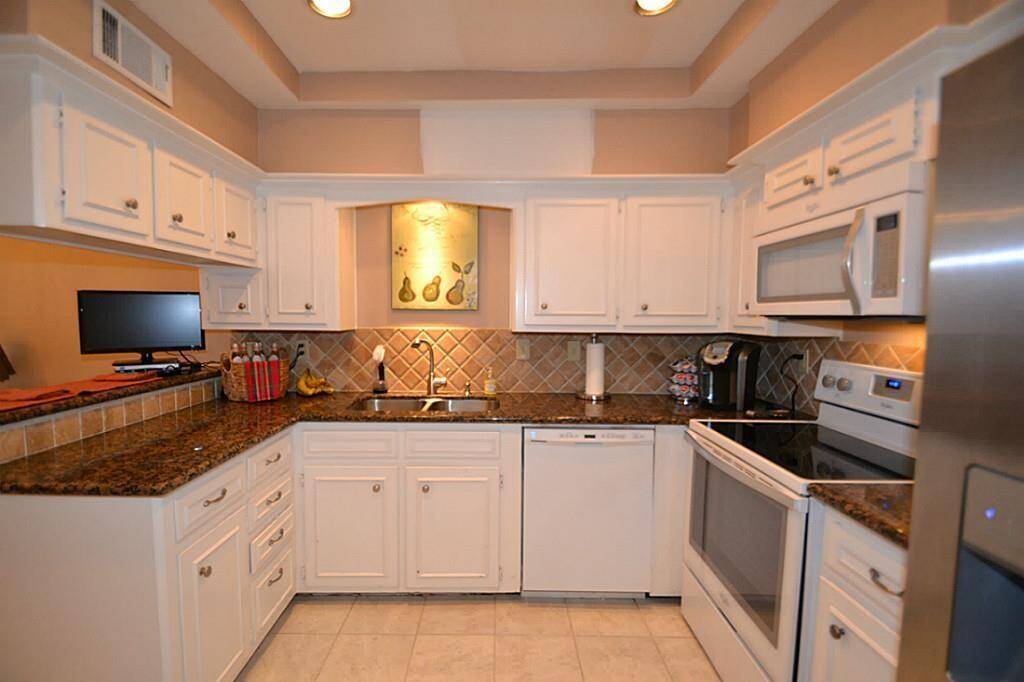 This kitchen features white cabinetry, granite countertops, and stainless steel appliances. It includes a tile backsplash, recessed lighting, and a cozy layout, with modern conveniences like a built-in microwave and dishwasher.