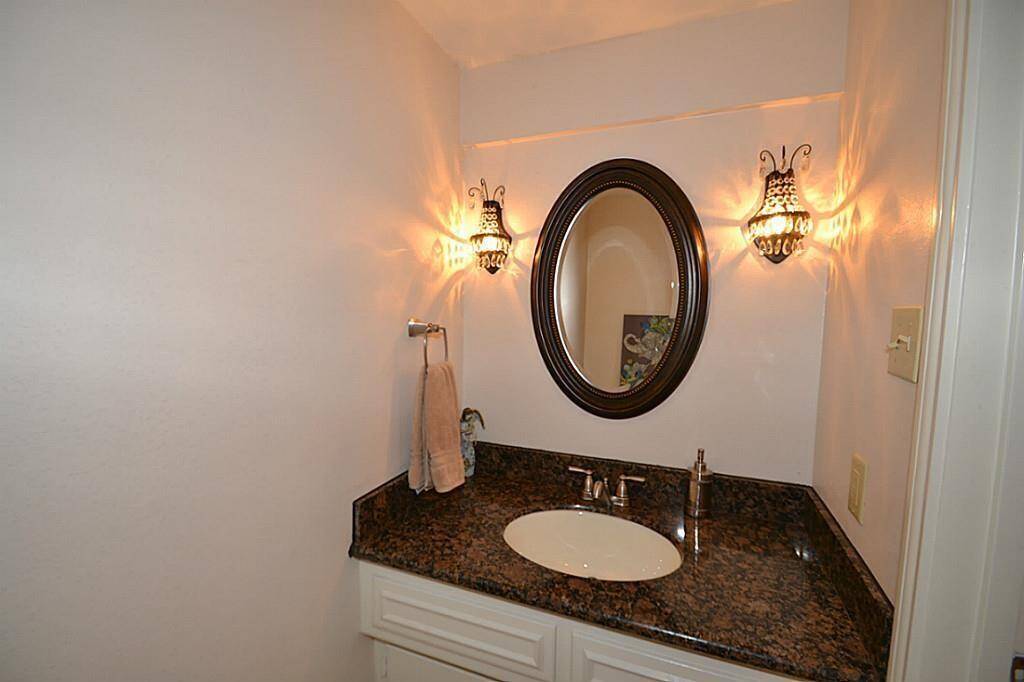 This photo shows a cozy bathroom with a granite countertop, an oval mirror, and elegant wall sconces providing warm lighting.