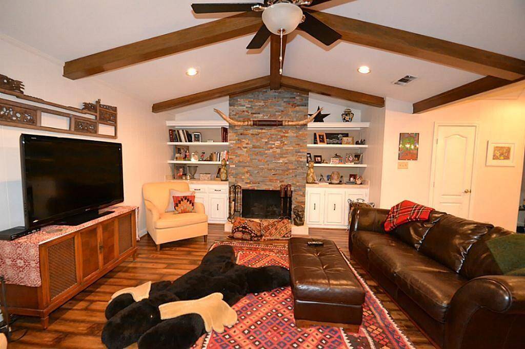 Cozy living room with vaulted ceiling and wooden beams, featuring a stone fireplace flanked by built-in shelves. Includes a large TV, leather sofa, and armchair, creating a warm and inviting atmosphere.