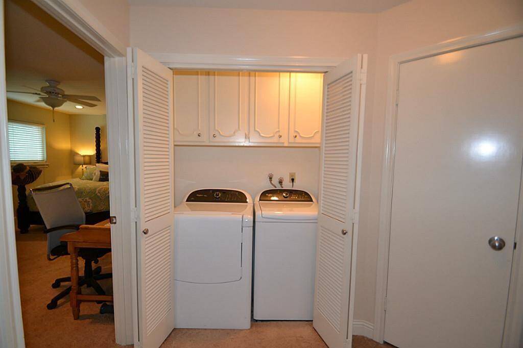 This photo shows a compact laundry area with a washer and dryer neatly tucked behind bi-fold doors. Adjacent to a bedroom, it features overhead storage cabinets for convenience.