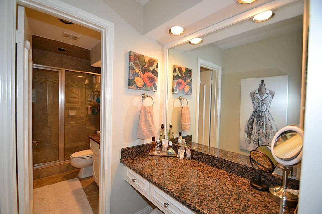 This photo shows a modern bathroom with a spacious granite countertop, large mirror, and recessed lighting. It features a glass-enclosed shower and tasteful decorative elements, creating a stylish and functional space.