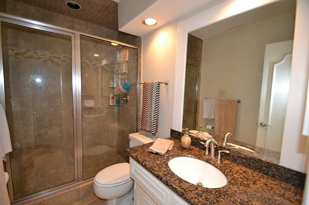 This is a modern bathroom featuring a glass-enclosed shower with tile accents, a granite countertop with an undermount sink, and contemporary fixtures. The warm lighting and neutral tones create a welcoming atmosphere.