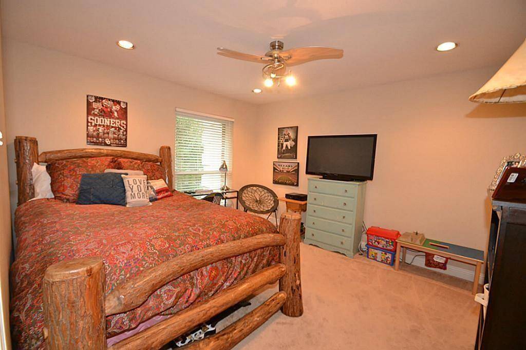Cozy bedroom with rustic log bed, ceiling fan, and carpeted floor. Features a large window for natural light, a TV on a dresser, and decorative sports-themed wall art. Ideal for a comfortable and personal retreat.
