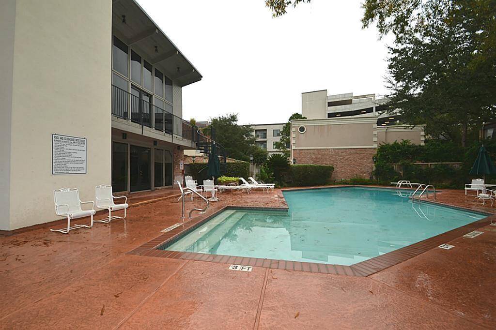 This photo shows a well-maintained swimming pool area with lounge chairs and a surrounding patio. It's adjacent to a mid-century style building with large windows, offering a relaxing outdoor space for residents.