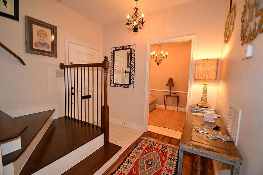This warm, inviting entryway features a wooden staircase, elegant chandelier, and decorative accents. A cozy hallway leads into a softly lit room, perfect for a welcoming atmosphere.