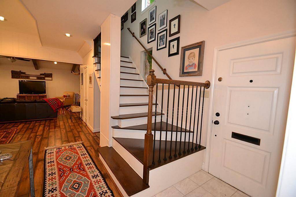 This welcoming entryway features a staircase with decorative railing, leading up to a well-lit gallery wall. The space opens to a cozy living area with warm wood floors and a comfortable layout.