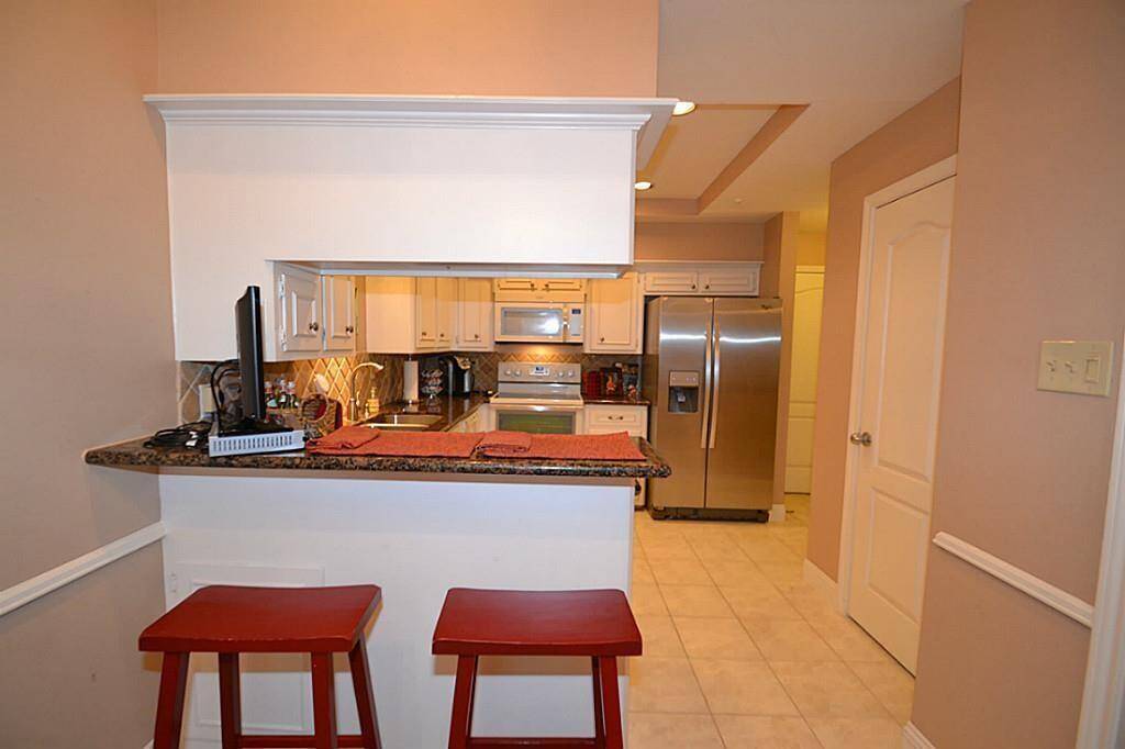 This photo showcases a cozy kitchen with a granite countertop bar, two red stools, stainless steel appliances, and white cabinetry. The space is well-lit with a warm, inviting ambiance.
