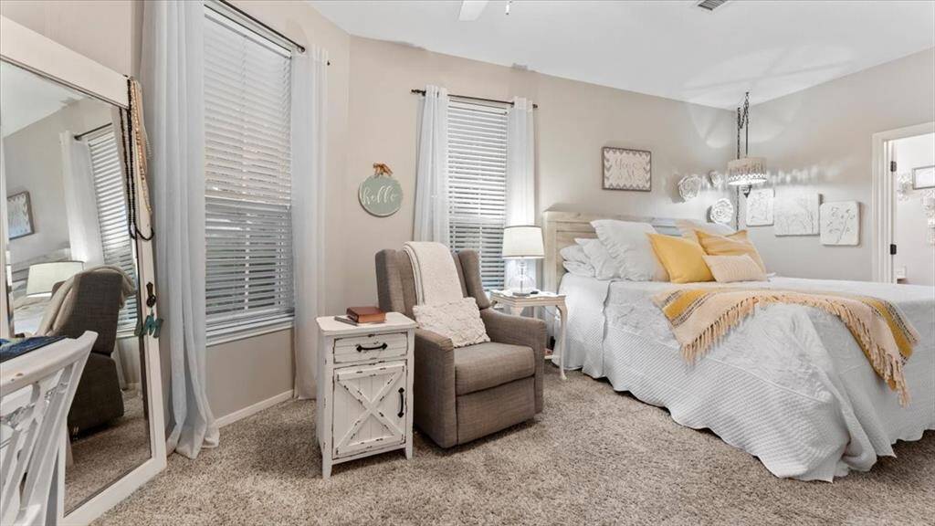The downstairs guest suite features a cozy, carpeted floor and soft, neutral tones. The room is well-lit with natural light from the windows.