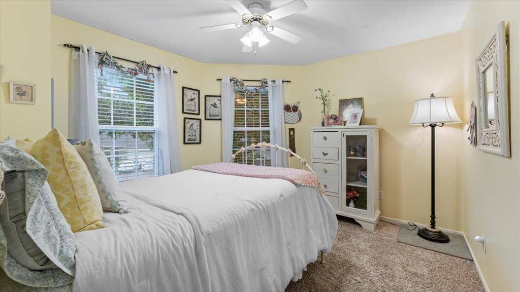 Cozy bedroom with rustic charm, featuring a shiplap accent wall and soft carpet flooring. The room is brightened by natural light from large windows, creating a quaint, inviting space.