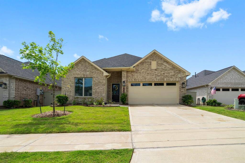 This charming brick home features a neatly manicured front yard, a young tree, and a spacious two-car garage. It offers a welcoming entrance and is set in a tidy, suburban neighborhood.