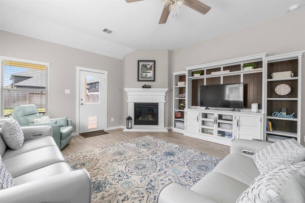 Bright and inviting living room with neutral tones, featuring a cozy fireplace and built-in entertainment center. Large windows provide natural light, while comfortable seating and a ceiling fan add to the relaxation ambiance. Perfect for gatherings and entertainment.