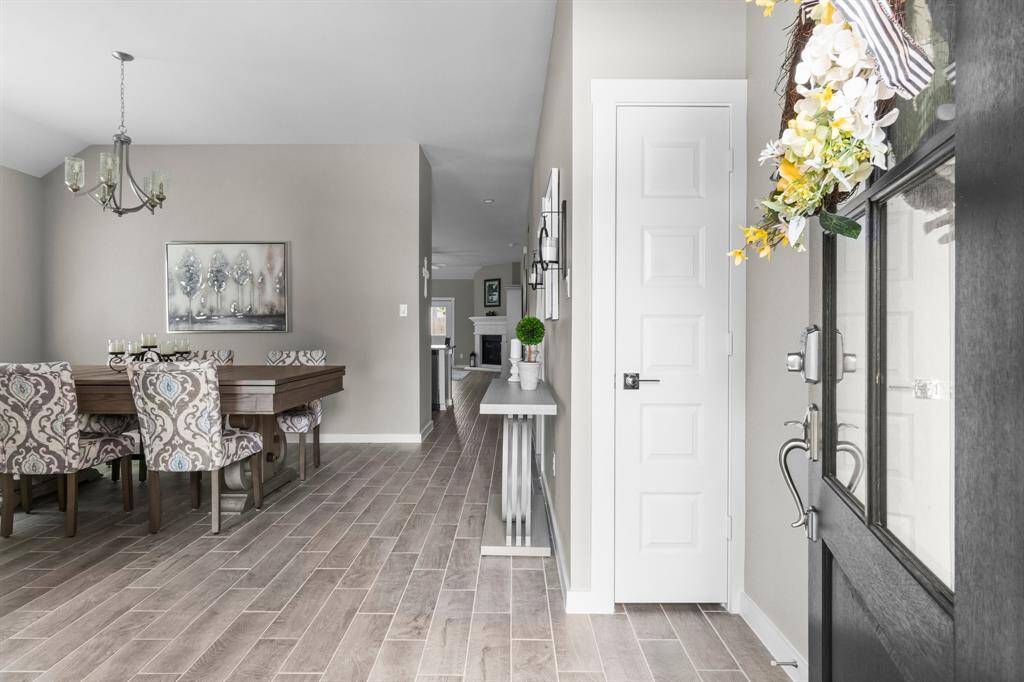 This photo showcases a bright, welcoming entryway leading to a dining area with elegant, patterned chairs and a modern chandelier. The space features light wood-look flooring and neutral walls, creating a warm and inviting atmosphere.