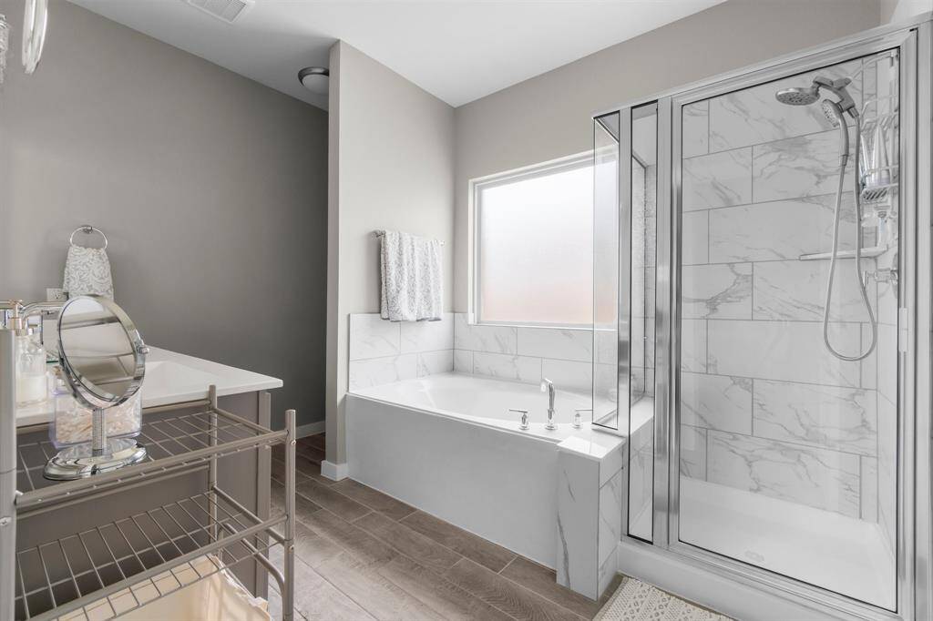 This bathroom features a modern design with a separate glass-enclosed shower, a spacious bathtub, and elegant tile work. The neutral color palette and large window provide a bright and airy feel.