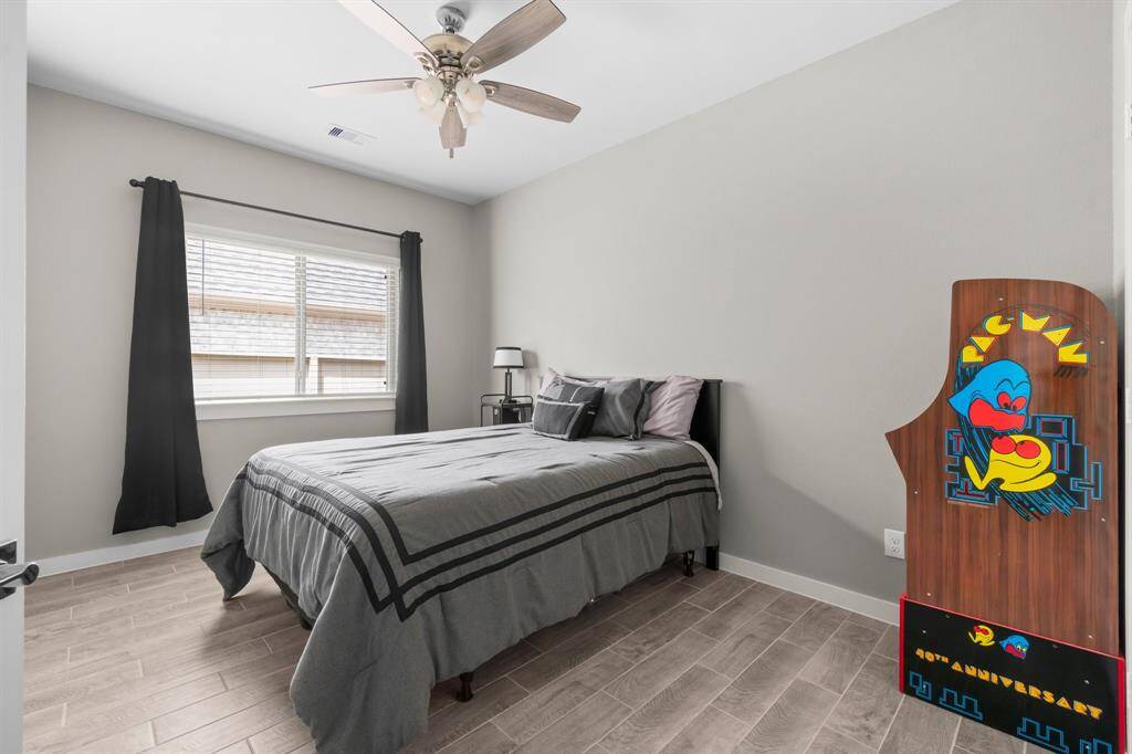 This bedroom is bright and cozy, featuring a large window and a ceiling fan, and wood-style style flooring.