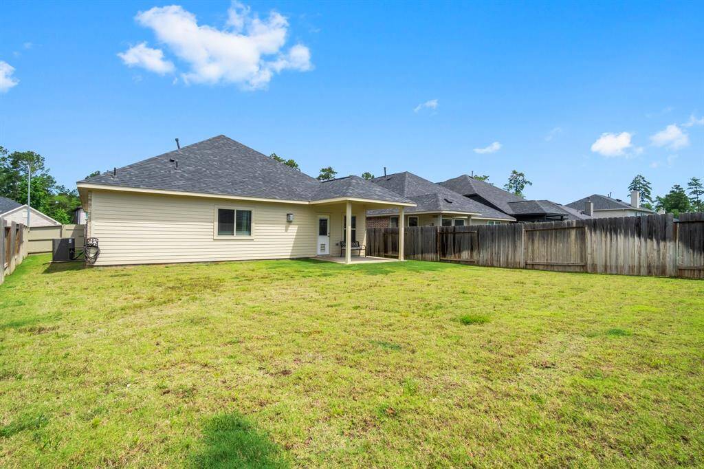 Spacious backyard with a well-maintained lawn, wooden fence for privacy, and a covered patio area attached to a single-story home. Ideal for outdoor activities and relaxation.