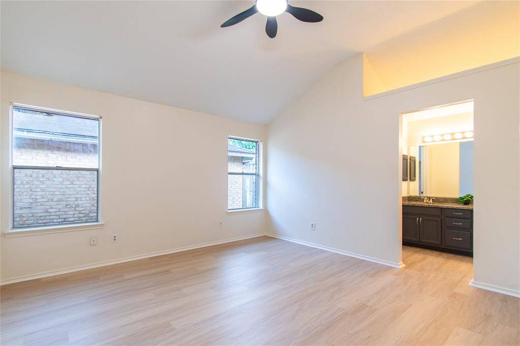 Primary bedroom features vinyl flooring, large windows, and a ceiling fan. It connects to a modern en-suite bathroom with dark cabinetry and ample lighting.