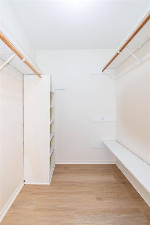 Walk-in closet with light vinyl flooring, double hanging rods, and built-in shelving for ample storage.