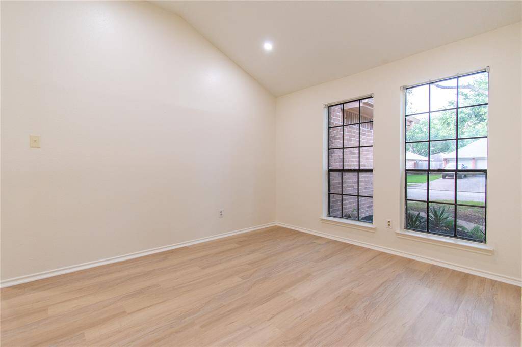 Bright, open space with light wood flooring and high ceilings. Two large windows provide ample natural light and a view of the outdoors, creating an inviting atmosphere.