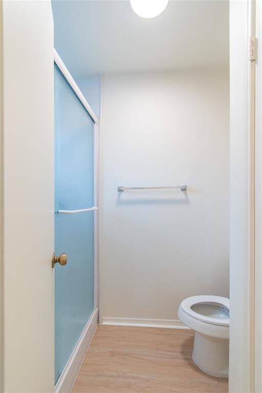 Bathroom features a shower with frosted glass doors, a toilet, and a towel rack. It has light walls and flooring, creating a bright and clean space.