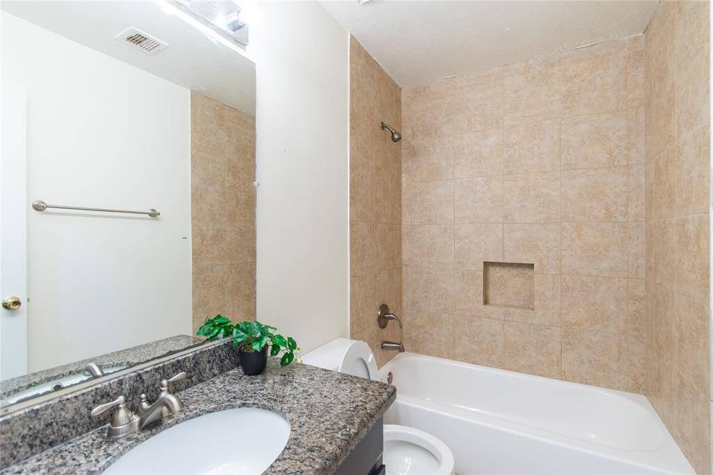 Bathroom features a sleek granite countertop with an undermount sink, complemented by a tiled shower and tub combo.