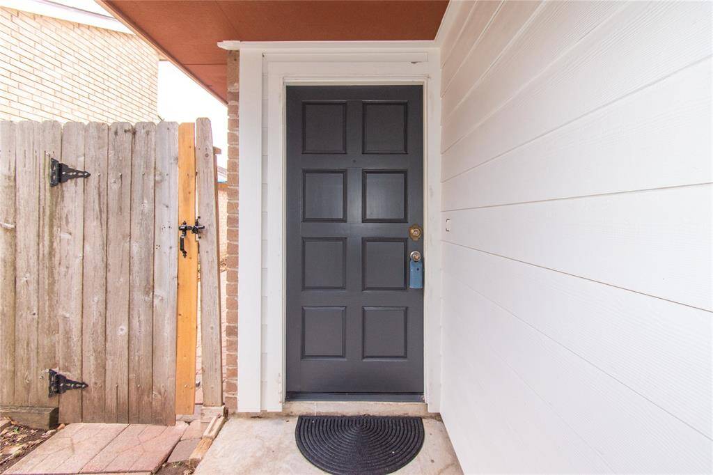 Dark front door and modern paneling. It features a wooden gate leading to a small, covered porch area with a simple doormat.