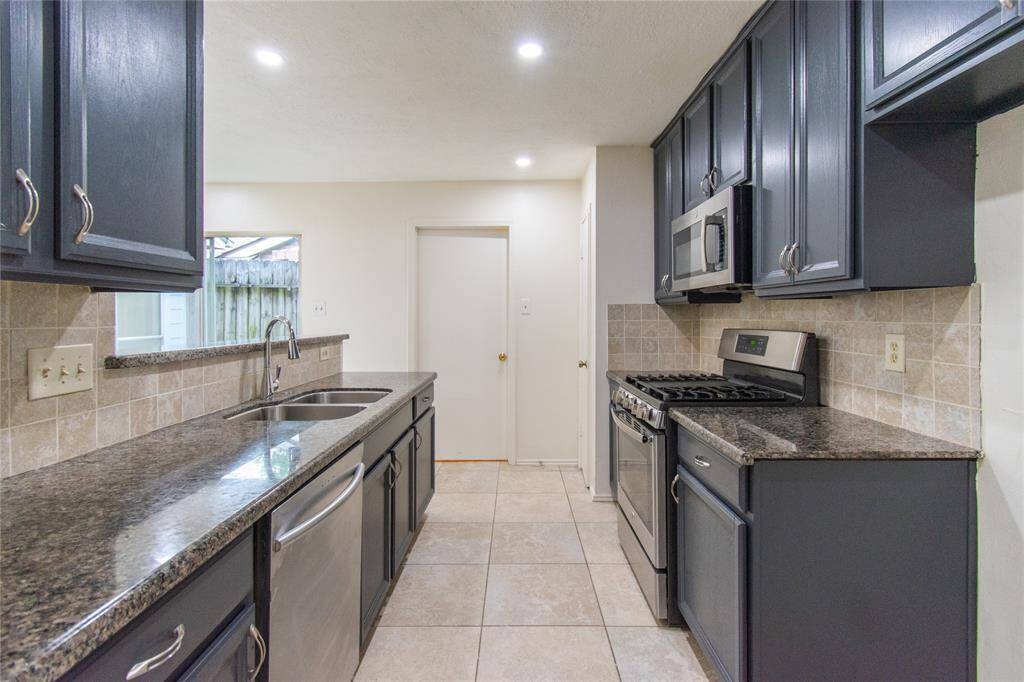 Modern kitchen with dark cabinetry, granite countertops, and stainless steel appliances. Features a sink, gas stove, and tiled backsplash. Bright and functional layout.