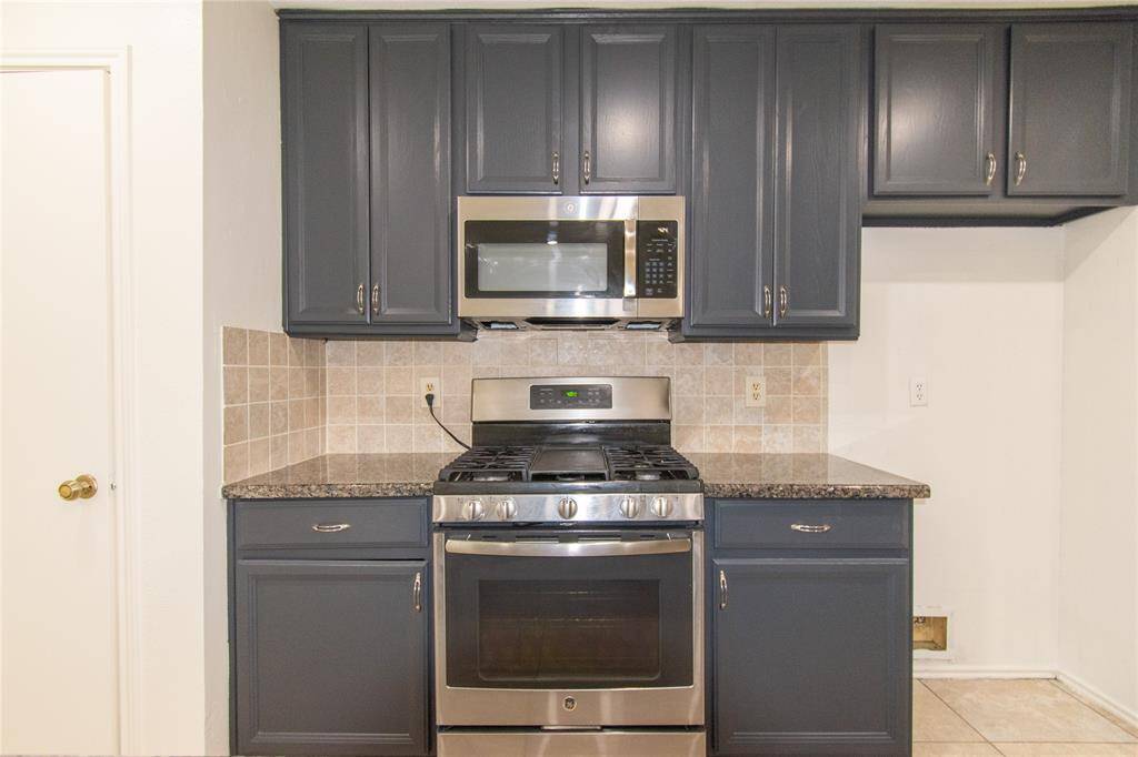Stainless steel gas stove and microwave, granite countertops, and a neutral tile backsplash, creating a stylish and functional cooking space.