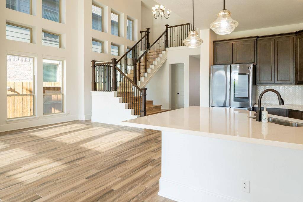 This bright and spacious home features an open floor plan with high ceilings and large windows, filling the space with natural light. The modern kitchen has dark wood cabinets and stainless steel appliances, while the elegant staircase adds a touch of sophistication. Perfect for entertaining and family living.