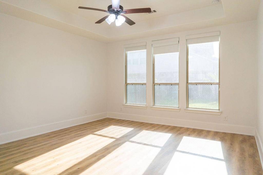 This bright room features large windows that let in plenty of natural light, a ceiling fan, and light wood flooring, creating a welcoming and airy atmosphere.