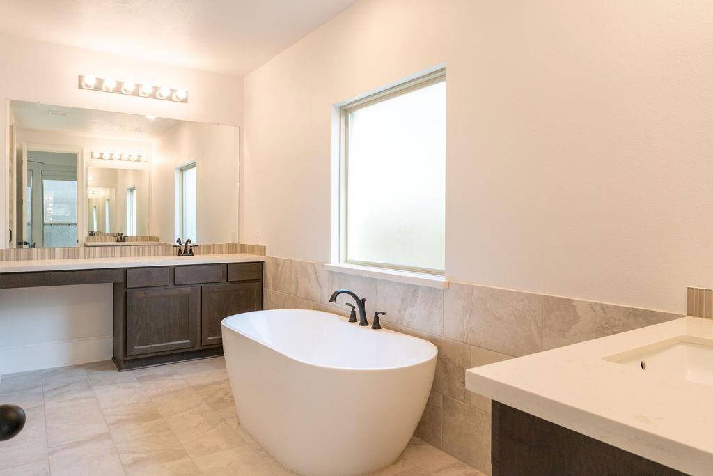 This bathroom features a modern design with a freestanding bathtub, a large mirror, and a spacious vanity with dark wood cabinets. It has a bright and airy feel, highlighted by a frosted window and sleek fixtures.