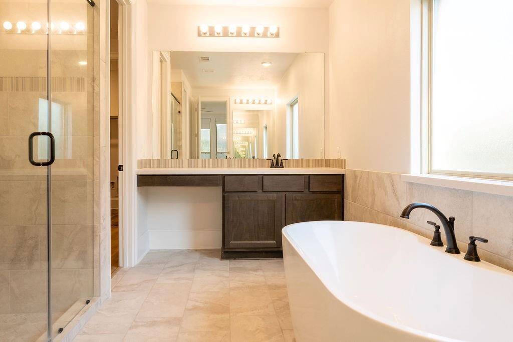 This bathroom features a spacious design with a glass-enclosed shower, large bathtub, and a modern vanity with ample storage. The neutral tones and abundant natural light create a serene atmosphere.