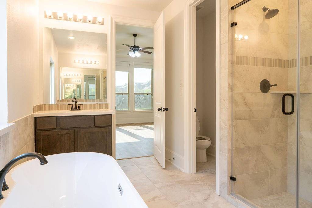 Bright, modern primary bathroom featuring a large glass-enclosed shower, a sleek freestanding bathtub, and a spacious vanity. The room is well-lit with natural light, creating an inviting, airy atmosphere.