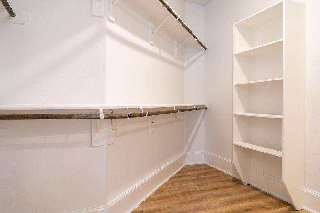 Spacious walk-in closet with wooden floors, multiple hanging rods, and built-in shelving, providing ample storage space.