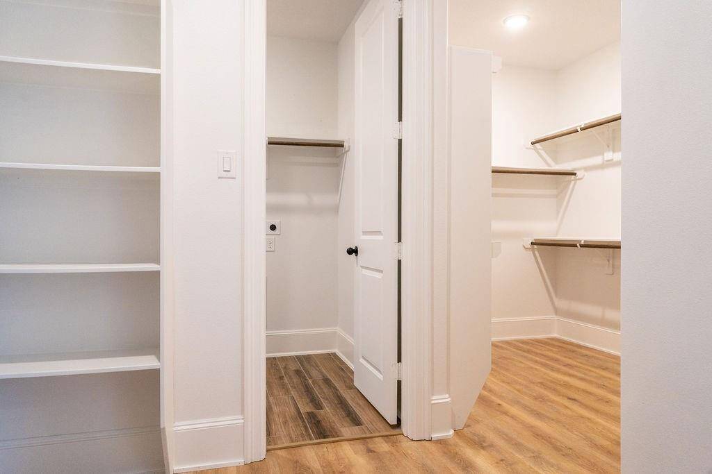 Spacious walk-in closet with wooden floors, built-in shelves, and ample hanging space. Bright and well-lit, ideal for storage and organization. The closet also connects to the laundry room!