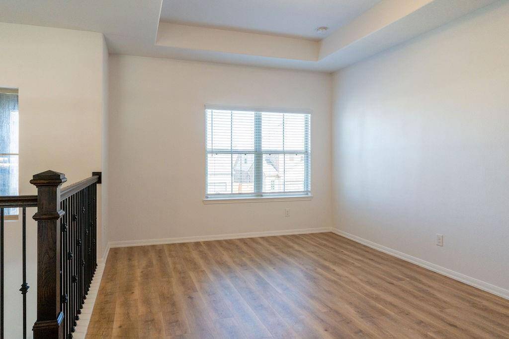 This bright room features large windows, light wood flooring, and a modern railing, creating an inviting open space ideal for a living area or office.