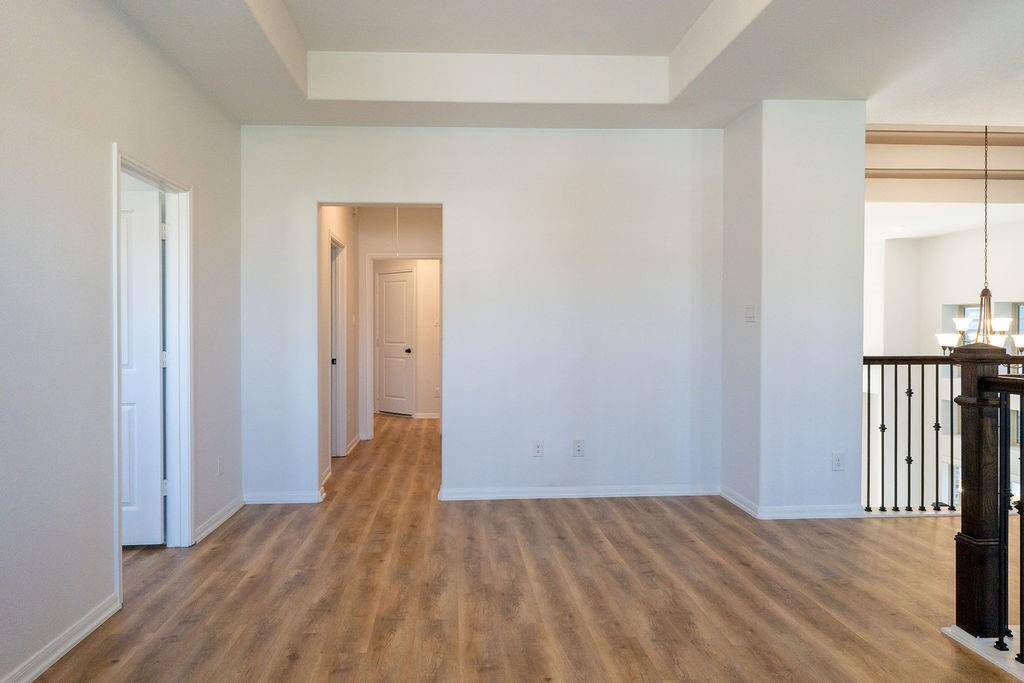 Bright, open living area with light wood flooring and neutral walls. The space includes a hallway leading to other rooms, and a railing overlooking a lower level, enhancing the open feel.