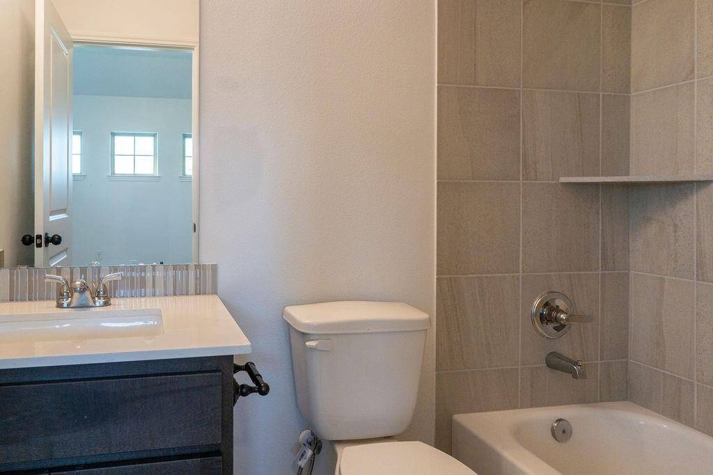 This bathroom features a modern design with neutral tiling, a white sink with a sleek faucet, a dark vanity cabinet, and a bathtub with a shower. It's well-lit with natural light from a nearby window.