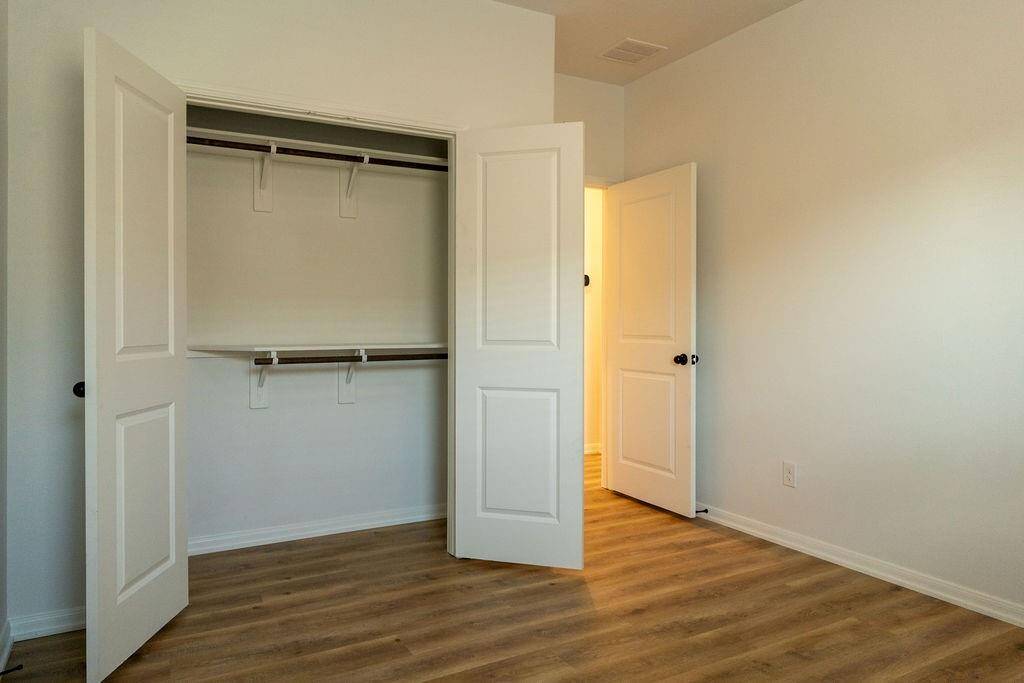 This room features a spacious closet with double doors and a built-in shelf, set against light-colored walls and wood flooring, offering a clean, modern look.